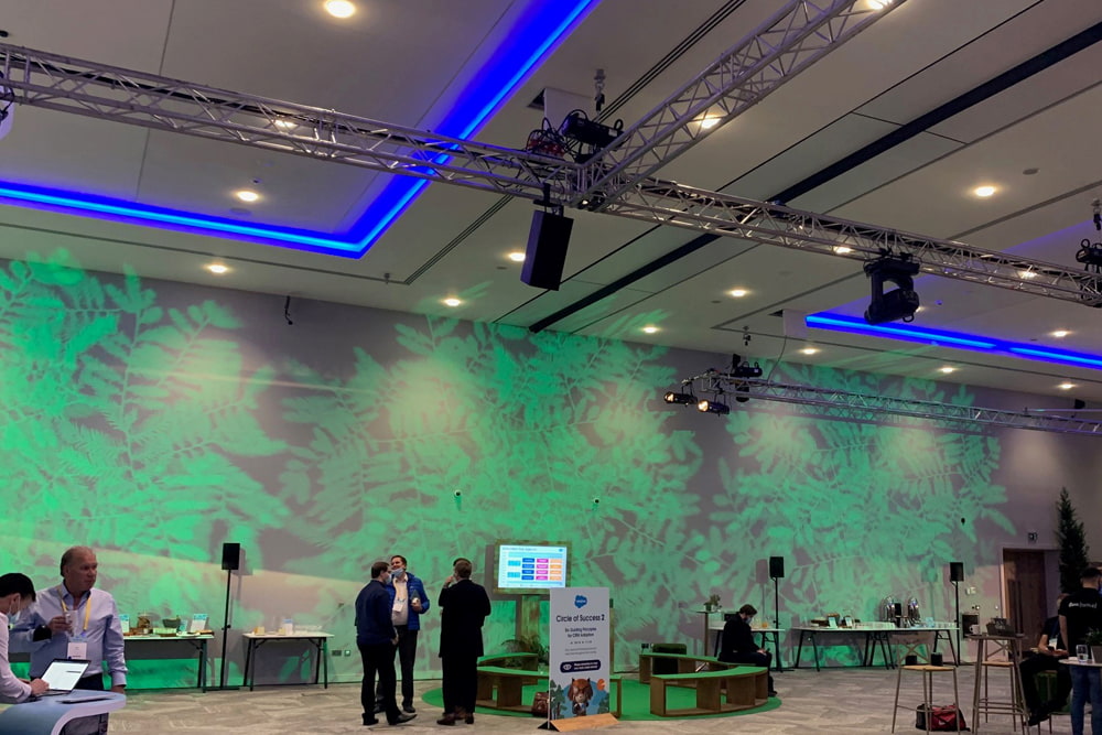 An event space with green projected leaves on the back wall and people stood in front of it