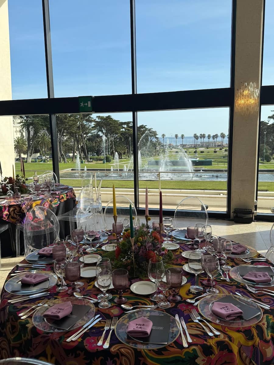 A round table decorated with candles and a tablecloth, fountains can be seen through the window