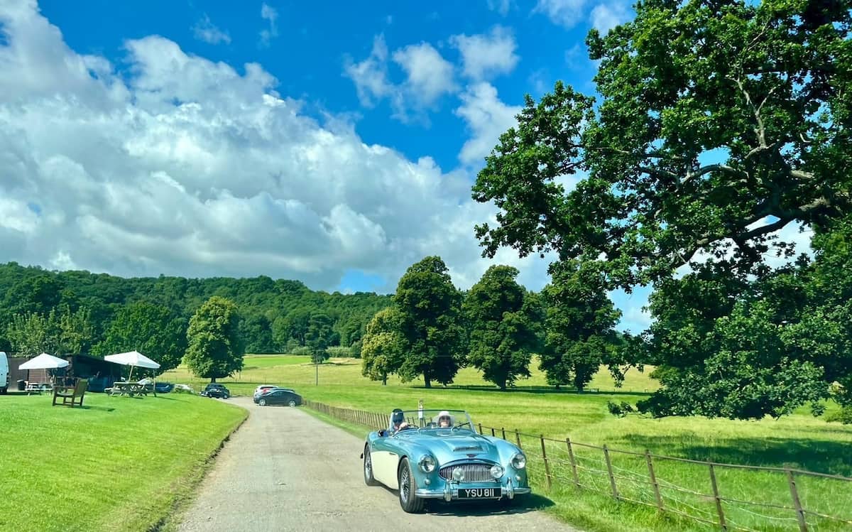 A blue convertible driving up a lane with fields either side